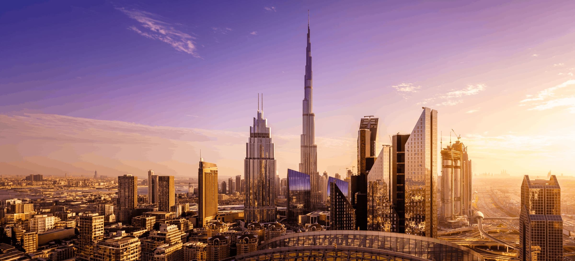 The Dubai skyline at sunset, with the Burj Khalifa rising above the surrounding towers.