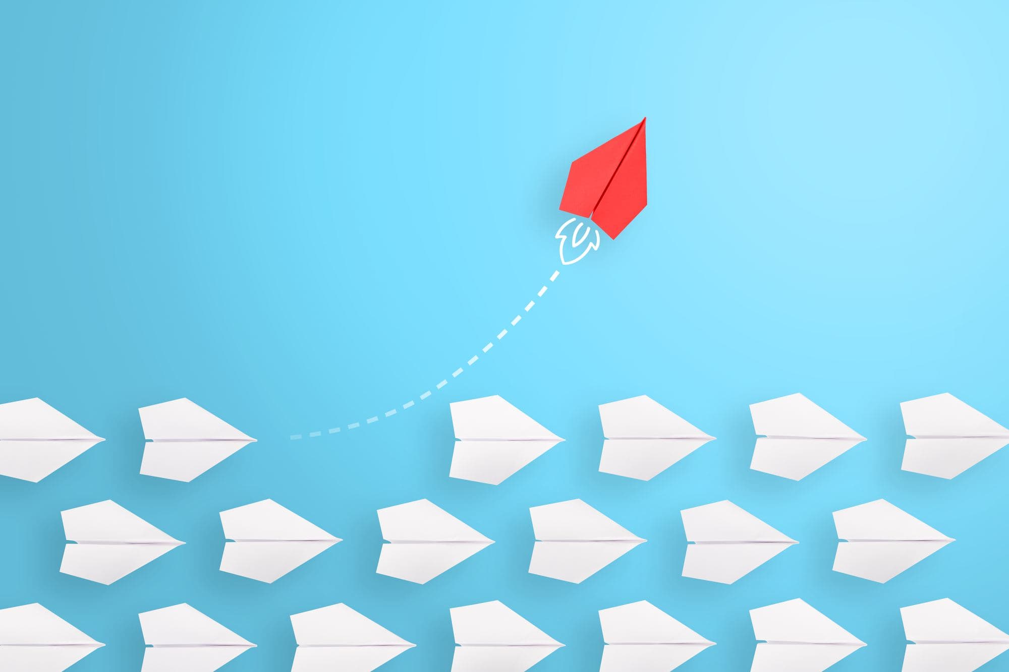 Paper planes flying in formation against a blue sky, with one red plane breaking away.